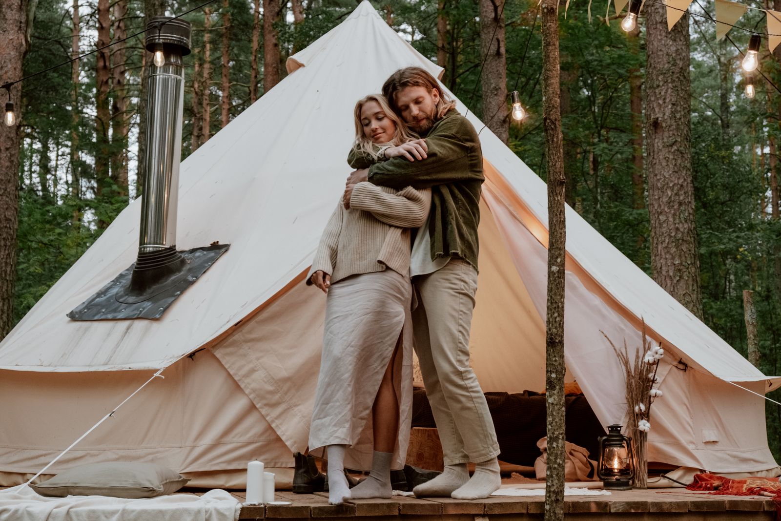 Zamilovaný pár objímající se před bílým glamping stanem v přírodě